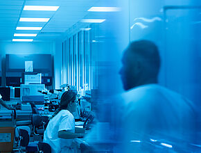Des techniciens de laboratoire au SUB à  travers une vitre bleue - Agrandir l'image (fenêtre modale)